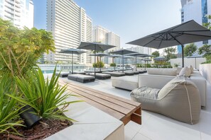 A rooftop lounge with outdoor seating, umbrellas, and a view of city buildings. - Free Housekeeping Visits During Your Stay - Stayshort - Modern 3 Bedroom in Business Bay That Sleeps 6 (Dubai)