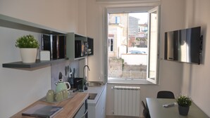 Eine kleine Küche mit Fenster, Heizkörper und einem an der Wand befestigten Flachbildfernseher.