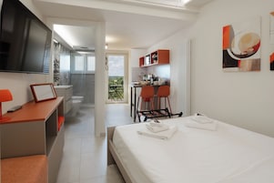 Habitación de hotel con cama, escritorio, televisor, balcón y kitchenette.