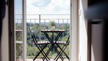 A balcony with a table and chairs, a potted plant, and a view of a green landscape.
