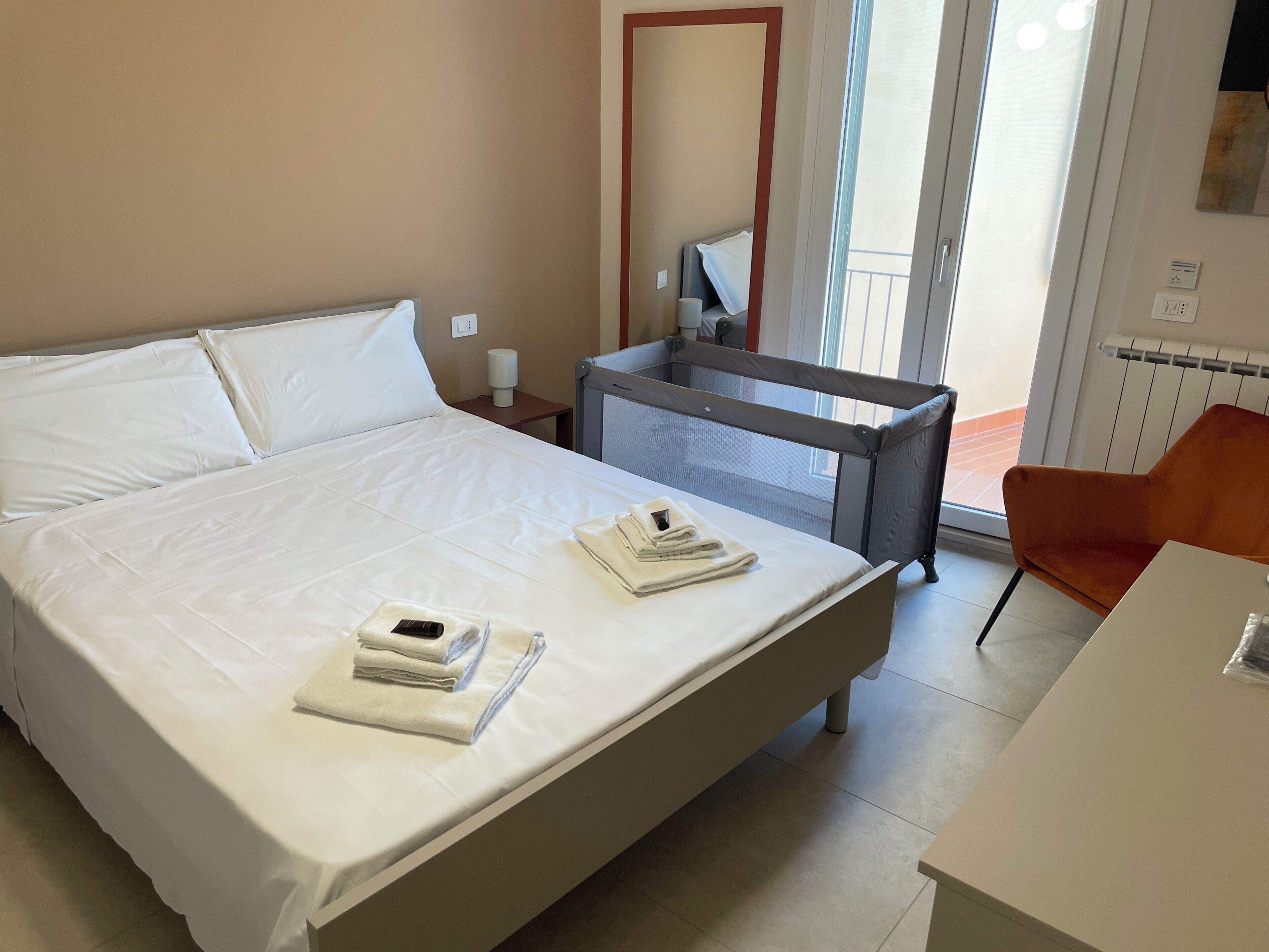 A hotel room with a bed, a desk, a chair, a window, and a door.