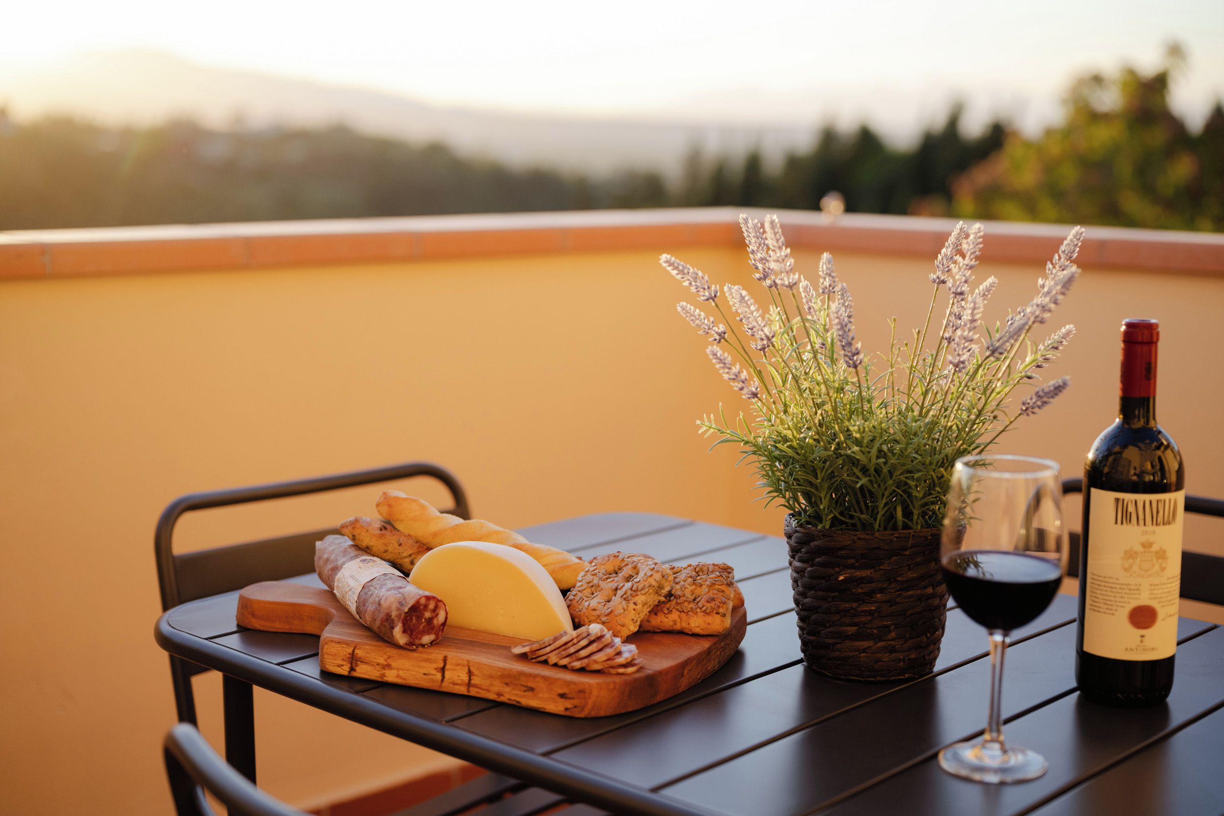 A table with a cheese board, bread, a bottle of wine, and a potted plant.