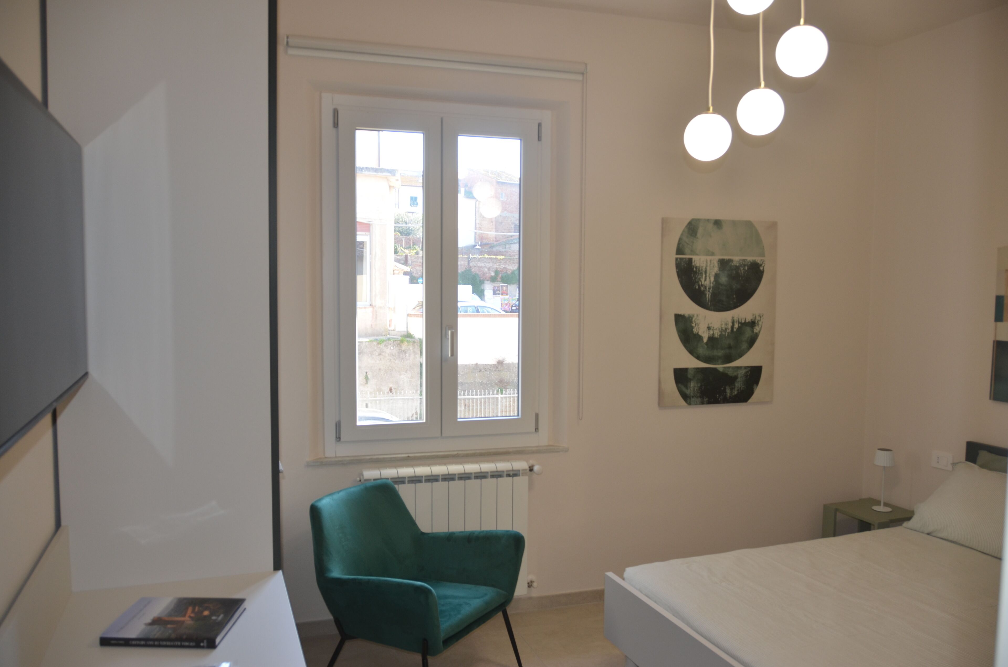 Un dormitorio con cama, una silla, radiador, ventana con vistas y decoración en la pared.