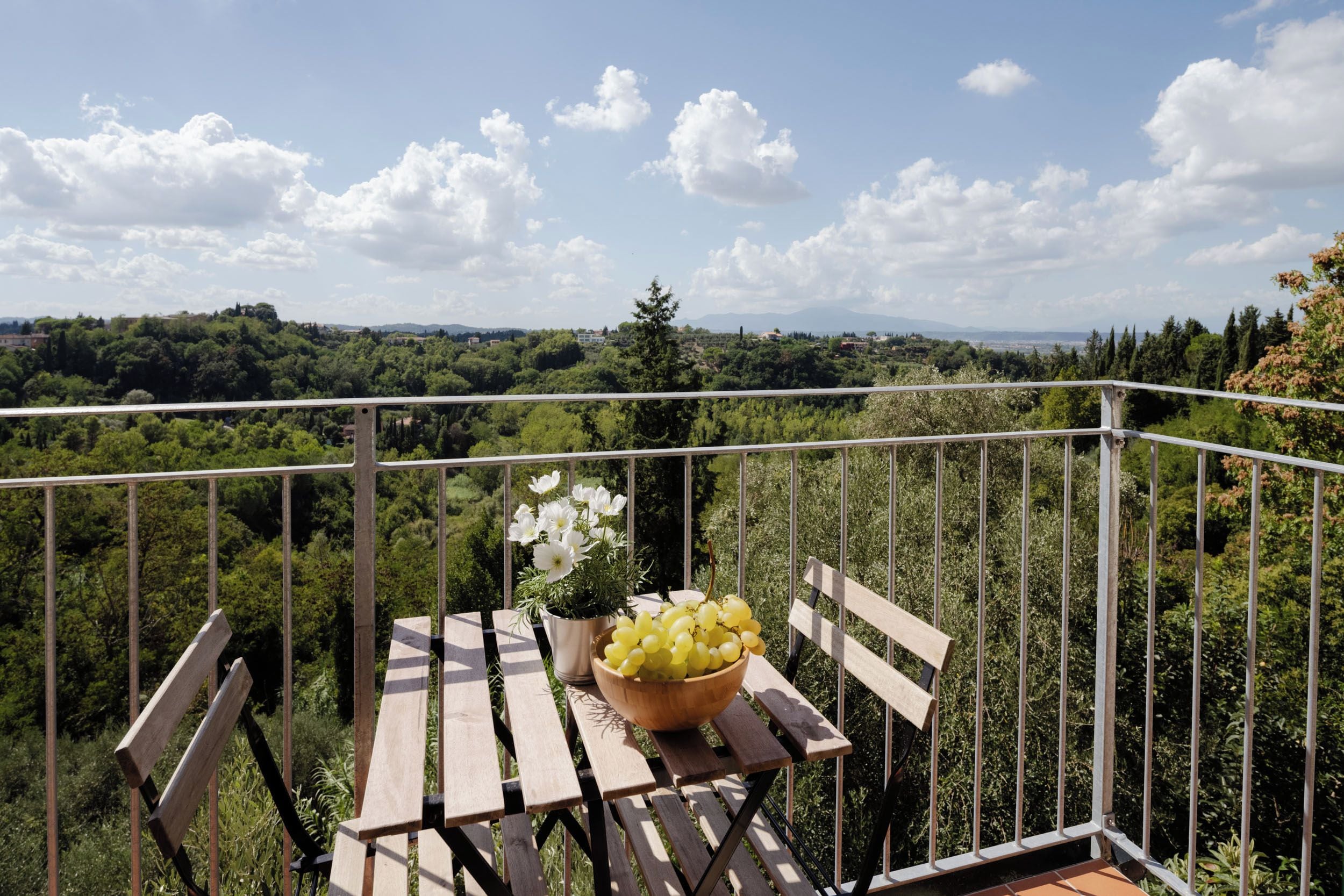 A balcony with a table, a bowl of grapes, and a potted plant with white flowers.