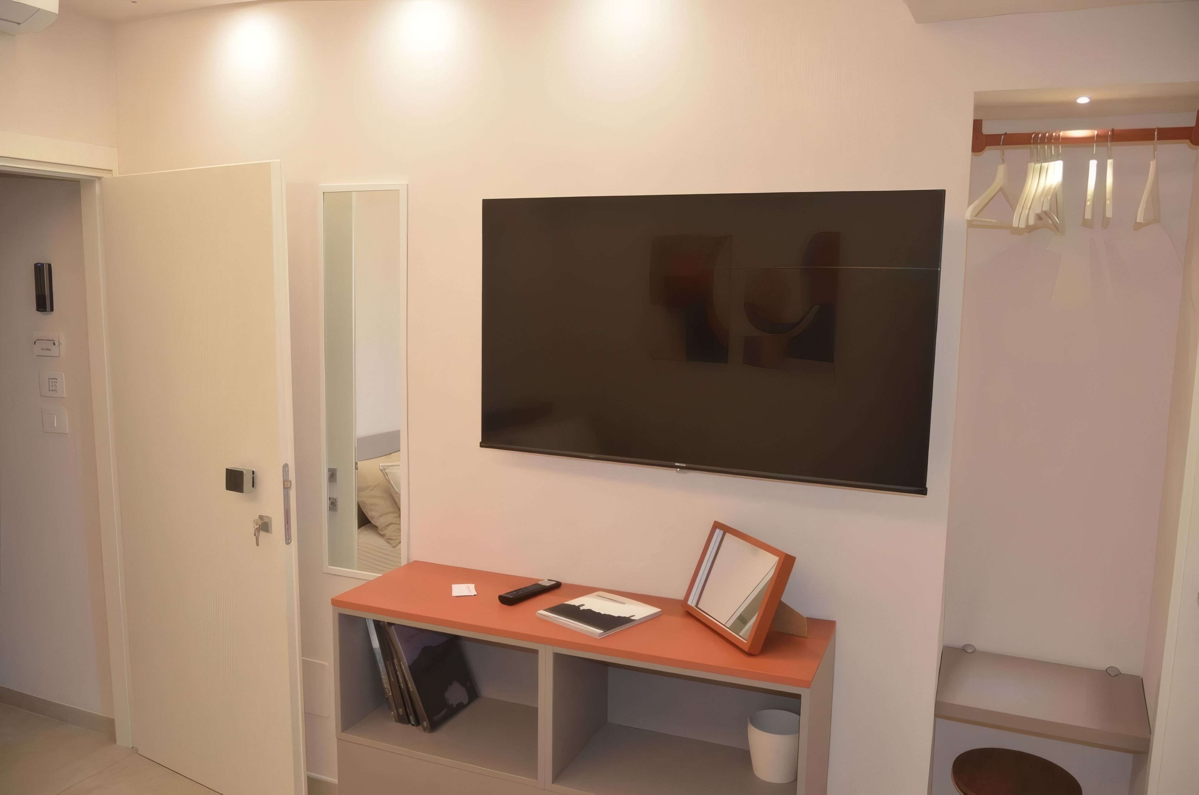 Une chambre d’hôtel dotée d’un grand téléviseur à écran plat fixé au mur, d’une petite console en bois sur laquelle repose une télécommande, d’un tableau encadré et d’un miroir.