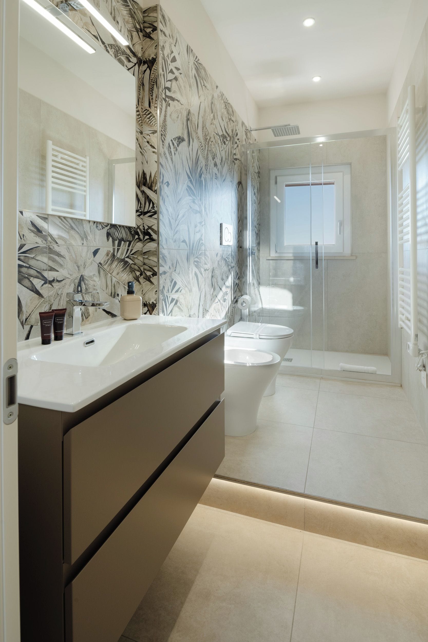 A modern bathroom with a large mirror, two sinks, a shower, and a toilet.