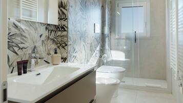 A modern bathroom with a large mirror, two sinks, a shower, and a toilet.