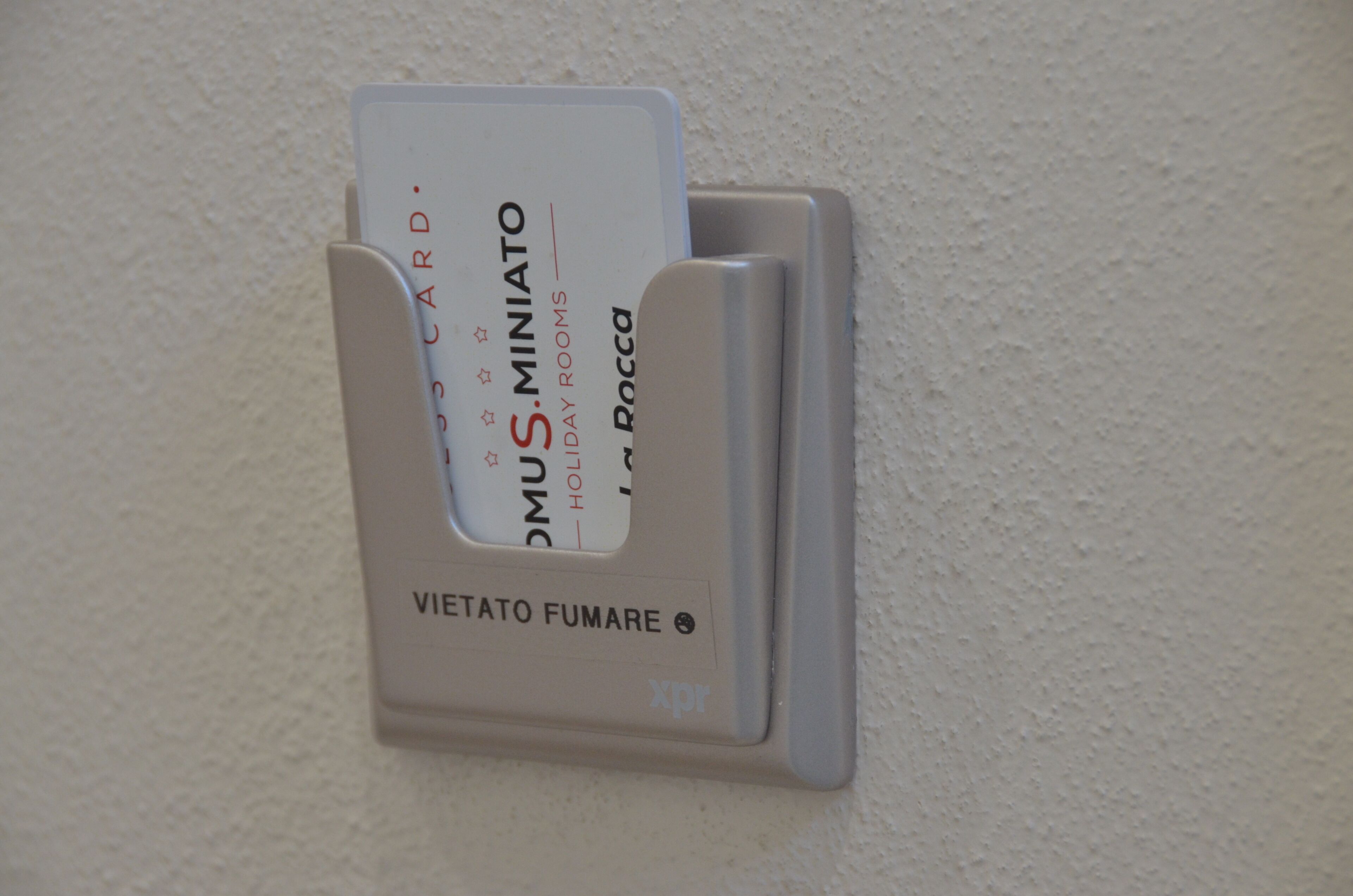 A card slot with a card inserted, labeled 'DOMUS MINIATO HOLIDAY ROCCA' and 'VIETATO FUMARE.'