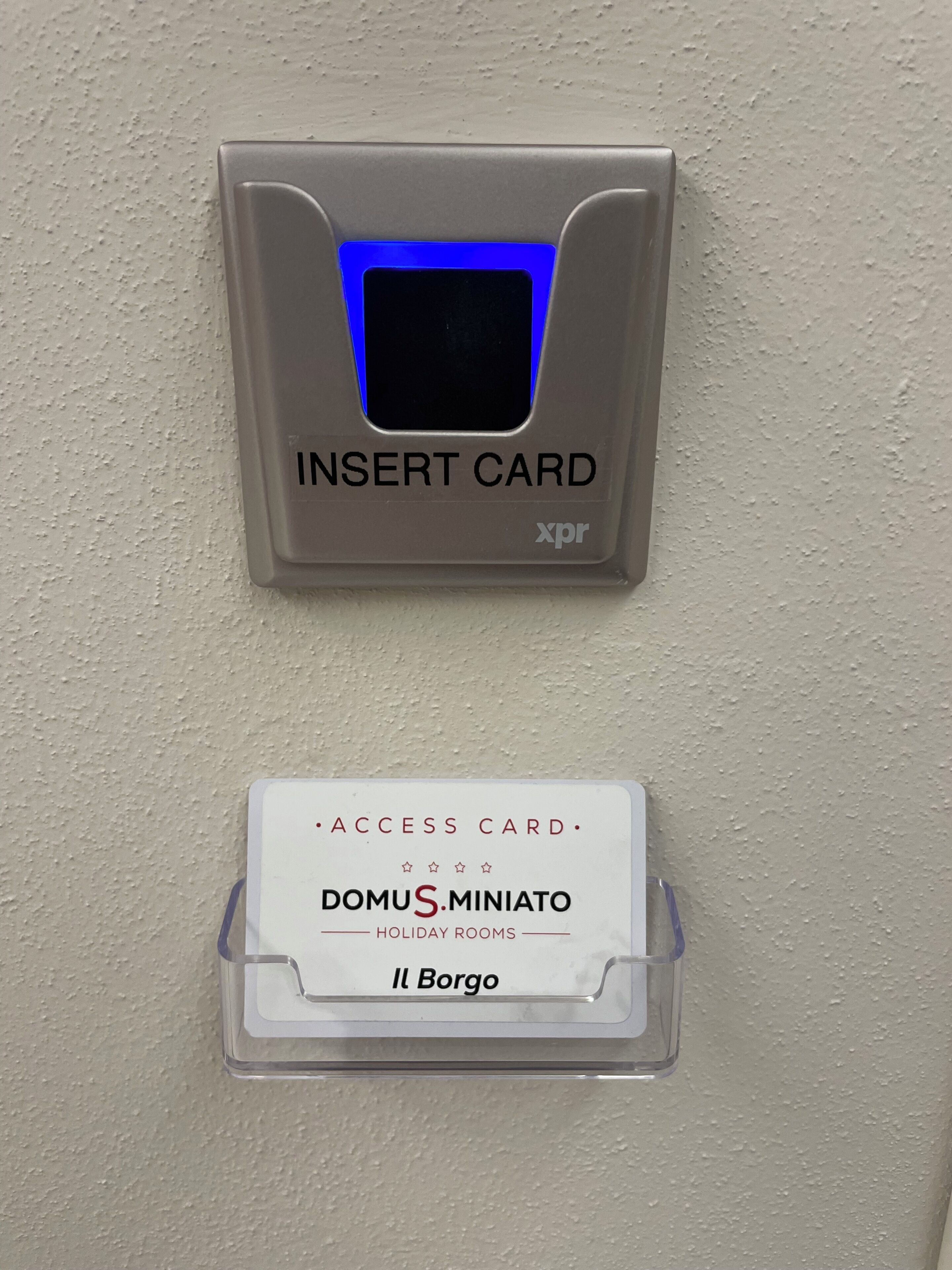 Un lector de tarjetas con una luz azul, una ranura para tarjetas y un cartel que dice 'DOMUS MINIATO HOLIDAY ROOMS Il Bargo'.