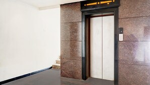 Un ascensor moderno con pared de mármol y estructura negra.