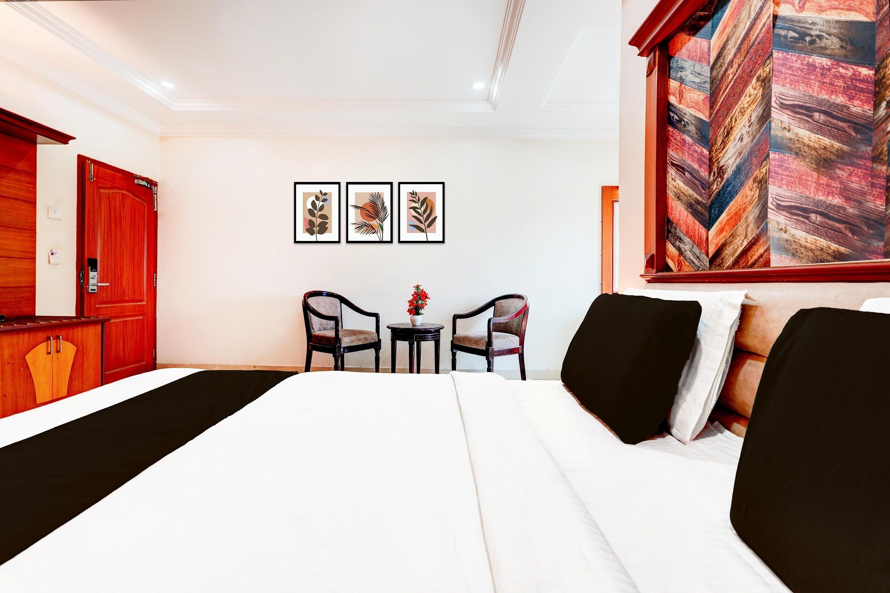A hotel room with a bed, two chairs, a small table with a vase, and three framed pictures on the wall.