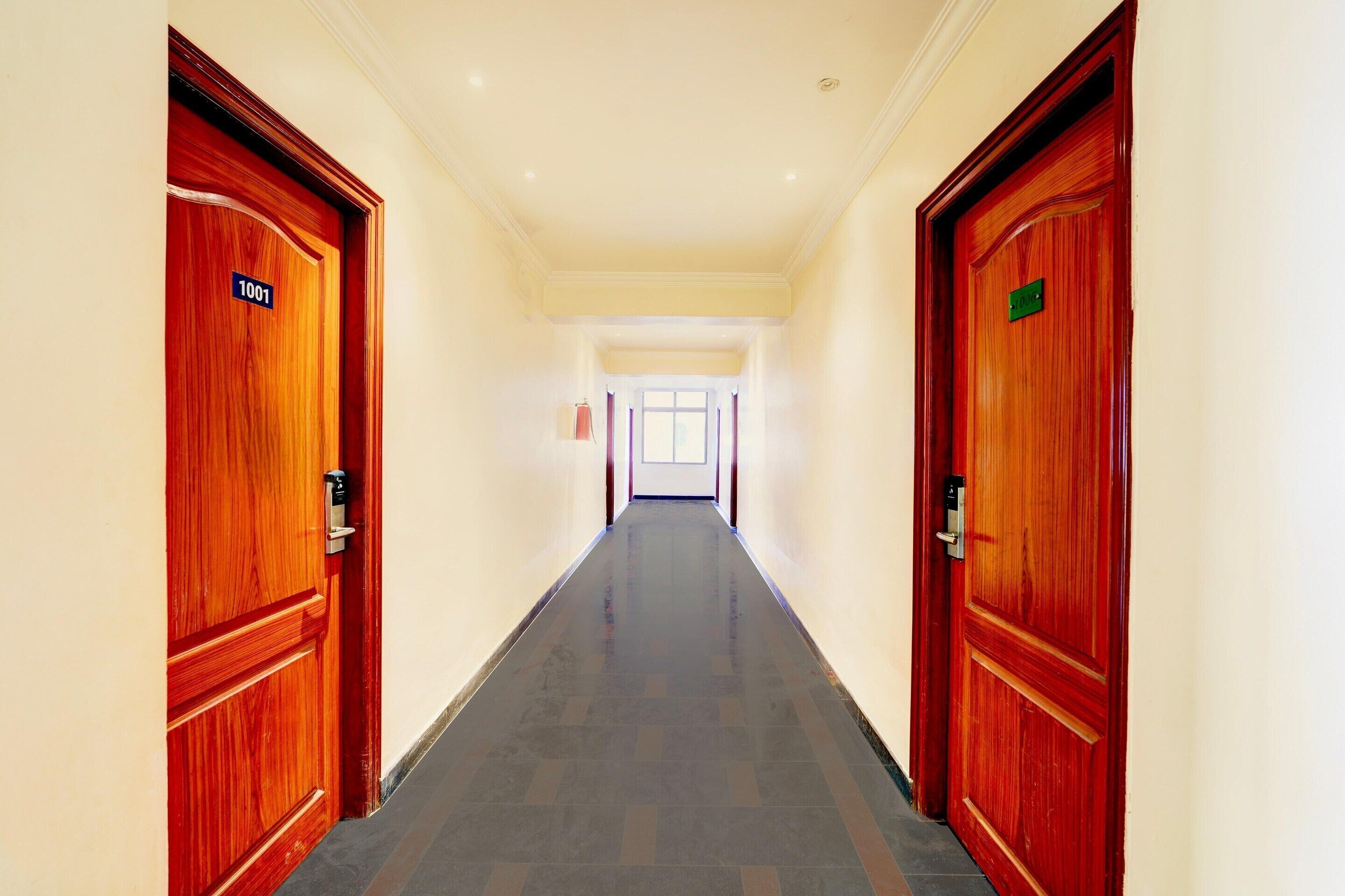 Un pasillo de hotel con puertas de madera, suelo de baldosas y un techo luminoso.