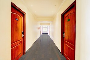 Corredor de hotel com portas de madeira, soalho em azulejos e teto bem iluminado.