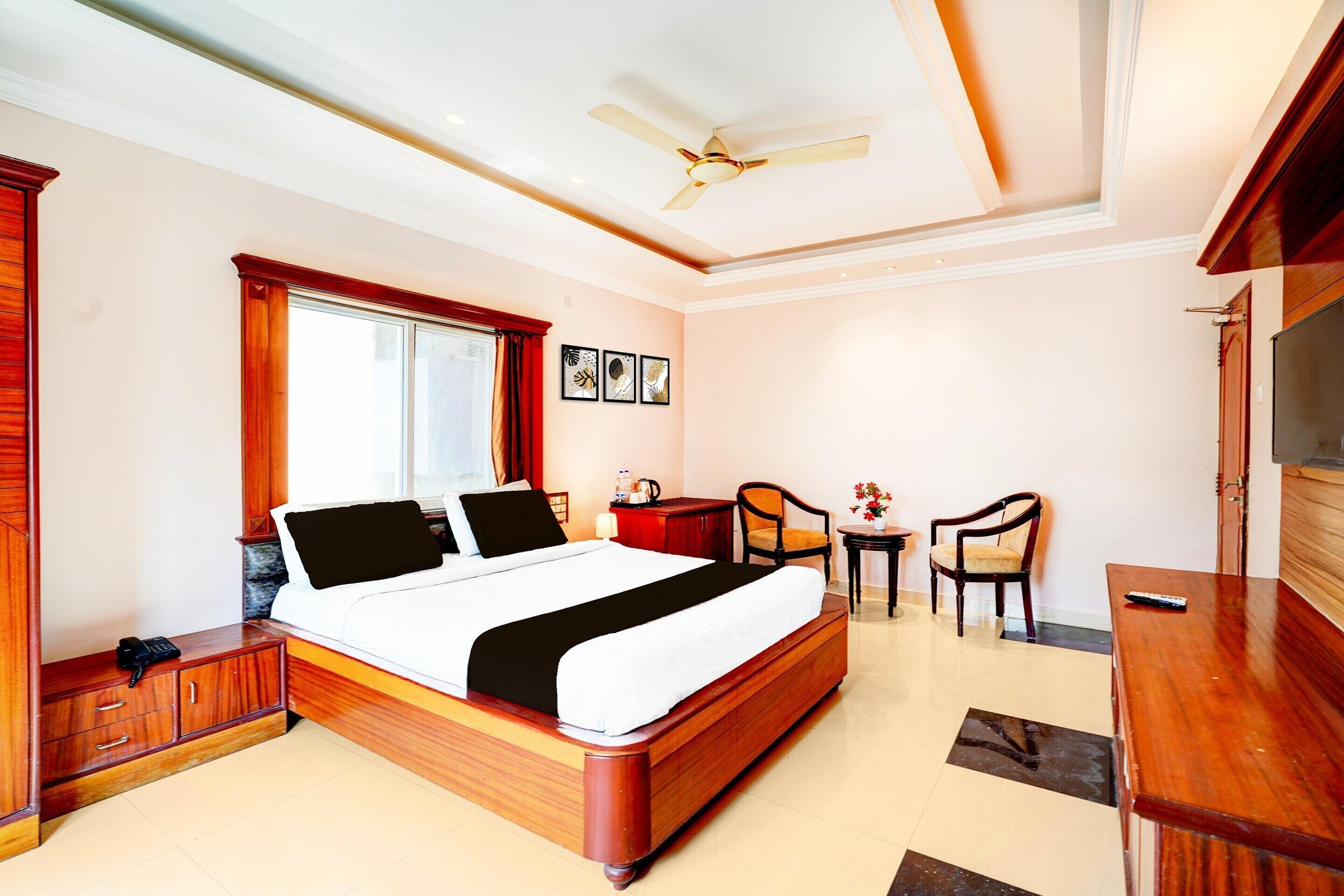Habitación de hotel con cama, escritorio, sillas, televisor, ventilador de techo y ventana.
