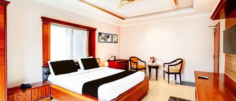 Habitación de hotel con cama, escritorio, sillas, televisor, ventilador de techo y ventana.