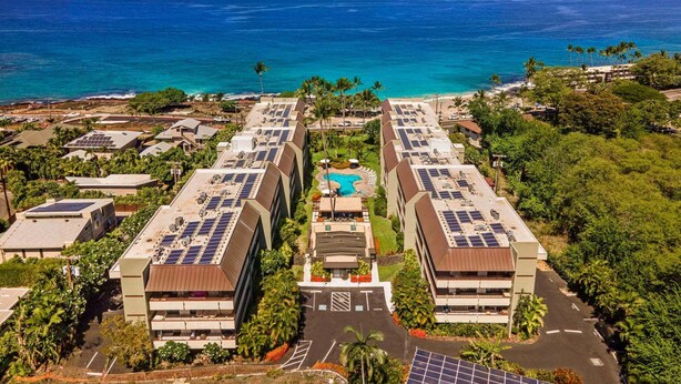 Un resort con varias edificaciones, paneles solares en los tejados, una piscina y vista al océano.