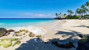 Una playa con agua turquesa cristalina, orilla de arena y un edificio con piscina.