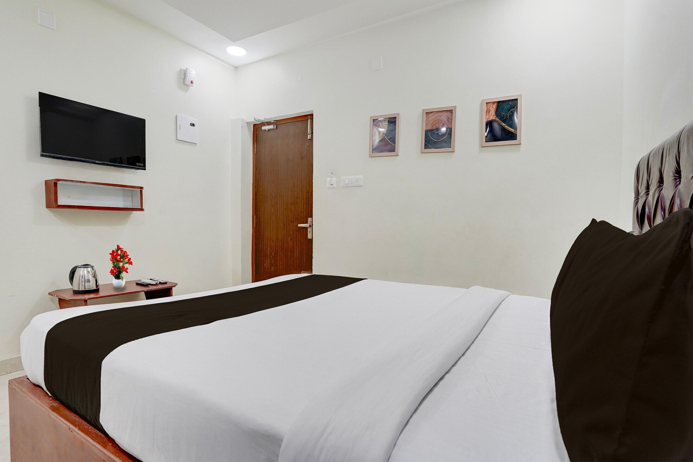 A hotel room with a bed, a television, a door, and a small table with a vase of flowers.