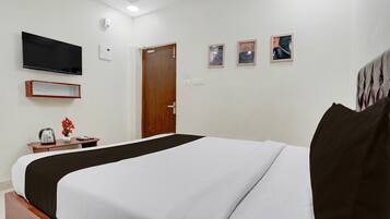 A hotel room with a bed, a television, a door, and a small table with a vase of flowers.