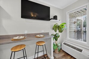 Cocina moderna con televisor de pantalla plana, dos taburetes de bar, una planta y una ventana con persianas.