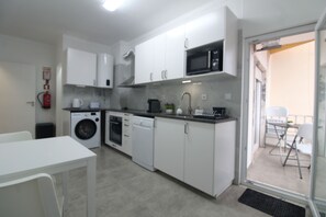 Une cuisine compacte avec des meubles blancs, un four à micro-ondes, un lave-linge et un coin repas comprenant une table et des chaises.