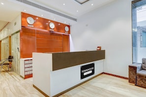 A reception desk with clocks displaying New York, New Delhi, and London times, a sign reading 'TOWNHOUSE Company Services,' and a seating area with a chair.