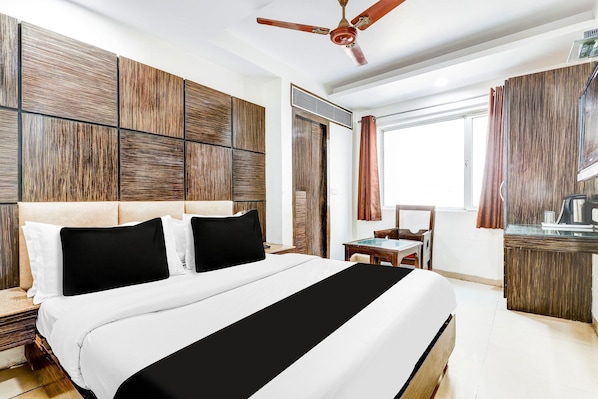 A hotel room with a bed, a desk, a chair, a ceiling fan, and a window with curtains.