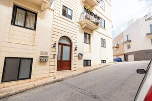 A building with a prominent arched entrance, a balcony with potted plants, and a mailbox on the ground floor. - budget apartment, affordable stay, cozy apartment, family friendly, group accommodation, patio apartment, outdoor space, free wifi, smart TV, kitchen, central location, value stay, comfortable stay (Il-Mellieħa)