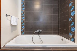A bathroom with a bathtub, a towel rack, and decorative tiles. - budget apartment, affordable stay, cozy apartment, family friendly, group accommodation, patio apartment, outdoor space, free wifi, smart TV, kitchen, central location, value stay, comfortable stay (Il-Mellieħa)