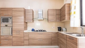 A modern kitchen with wooden cabinets, a microwave, a stove, and a sink. - budget apartment, affordable stay, cozy apartment, family friendly, group accommodation, patio apartment, outdoor space, free wifi, smart TV, kitchen, central location, value stay, comfortable stay (Il-Mellieħa)