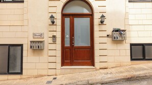 A building with a large arched wooden door, a mailbox, and two wall-mounted light fixtures. - budget apartment, affordable stay, cozy apartment, family friendly, group accommodation, patio apartment, outdoor space, free wifi, smart TV, kitchen, central location, value stay, comfortable stay (Il-Mellieħa)