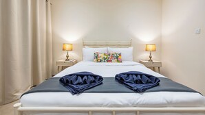 Un letto ben rifatto con due cuscini, due lampade da comodino e un cuscino decorativo su una testiera bianca.