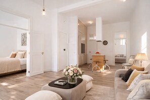 Ein modernes Wohnzimmer mit einer Couch, einem Couchtisch mit einer Vase, einem Essbereich mit Tisch und Stühlen sowie einer Küche im Hintergrund.