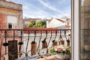 Ein Balkon mit schmiedeeisernem Geländer, einem Topf mit Blumen und Blick auf Gebäude mit roten Ziegeldächern.