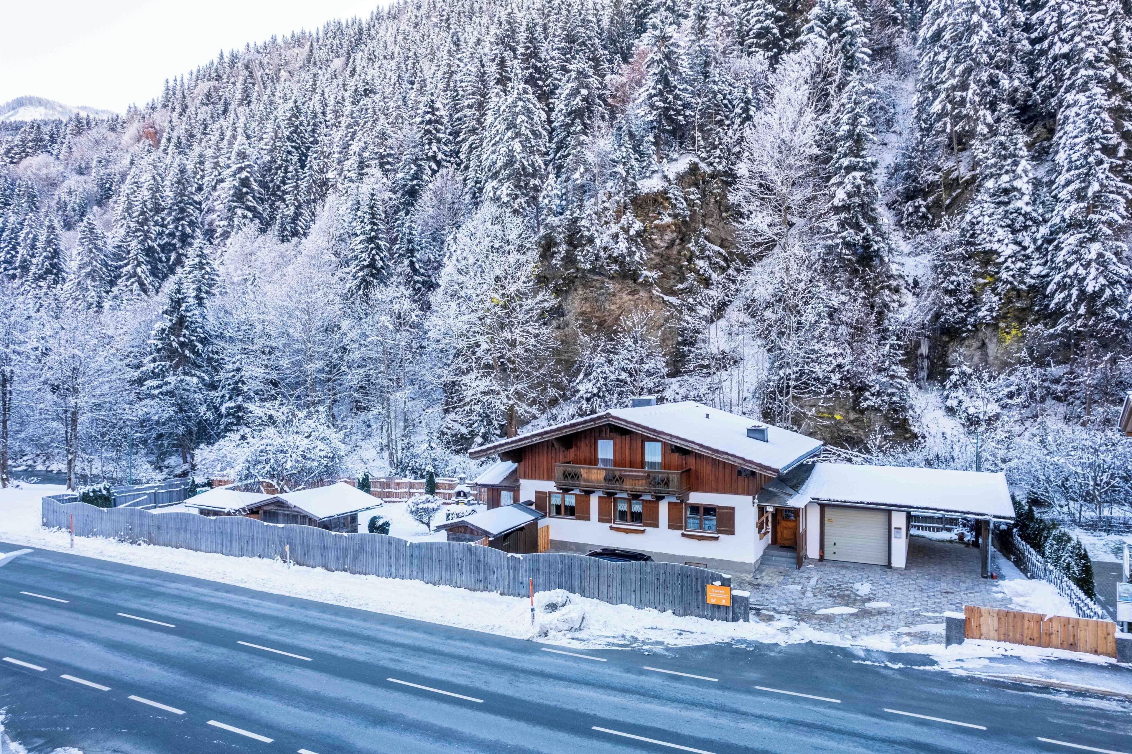 A snow-covered lodge with a wooden exterior, a garage, and a view of a snowy forest.