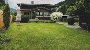 Une maison en bois avec un porche abrité, une pelouse bien entretenue et un petit jardin agrémenté d’un arbre en fleurs.