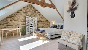 Camera da letto con soffitto spiovente, parete in pietra, un letto con lenzuola fantasia, un divano, una scrivania e una pianta decorativa.