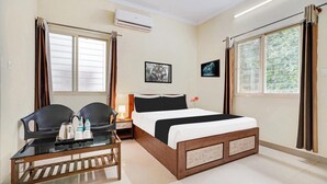 A hotel room with a bed, two chairs, a small table with a tray, an air conditioner, and two windows with curtains. - Deluxe Hebbal Mysore Green Orchid Resort (Mysore)