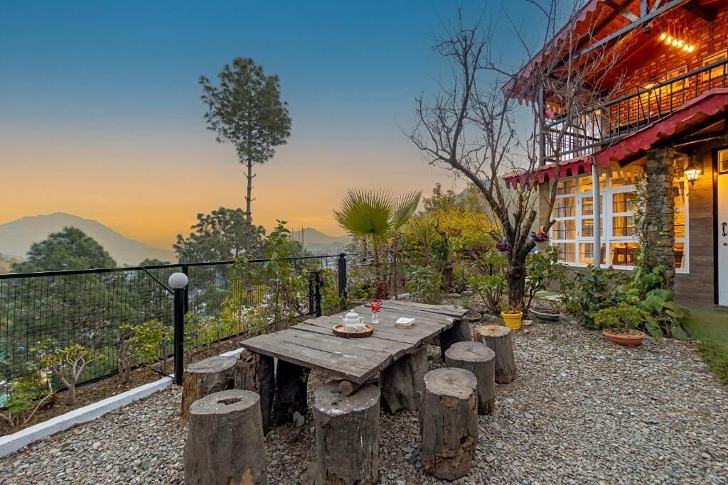 A wooden table with a vase and tray set outdoors, surrounded by trees and a view of mountains.