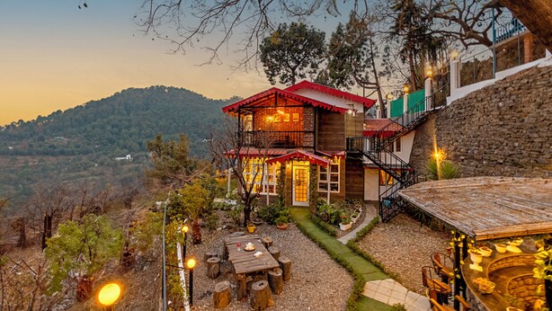 A rustic wooden house with a red roof, a stone staircase, and a patio area with a table and chairs. - Alaya Stays Farsauli 1 Pet friendly 3BHK (Nagri Gaon)