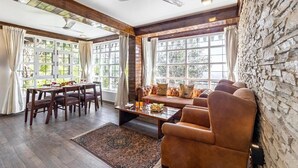 A room with a dining table, chairs, a sofa, a coffee table, and a stone wall. - Alaya Stays Farsauli 1 Pet friendly 3BHK (Nagri Gaon)