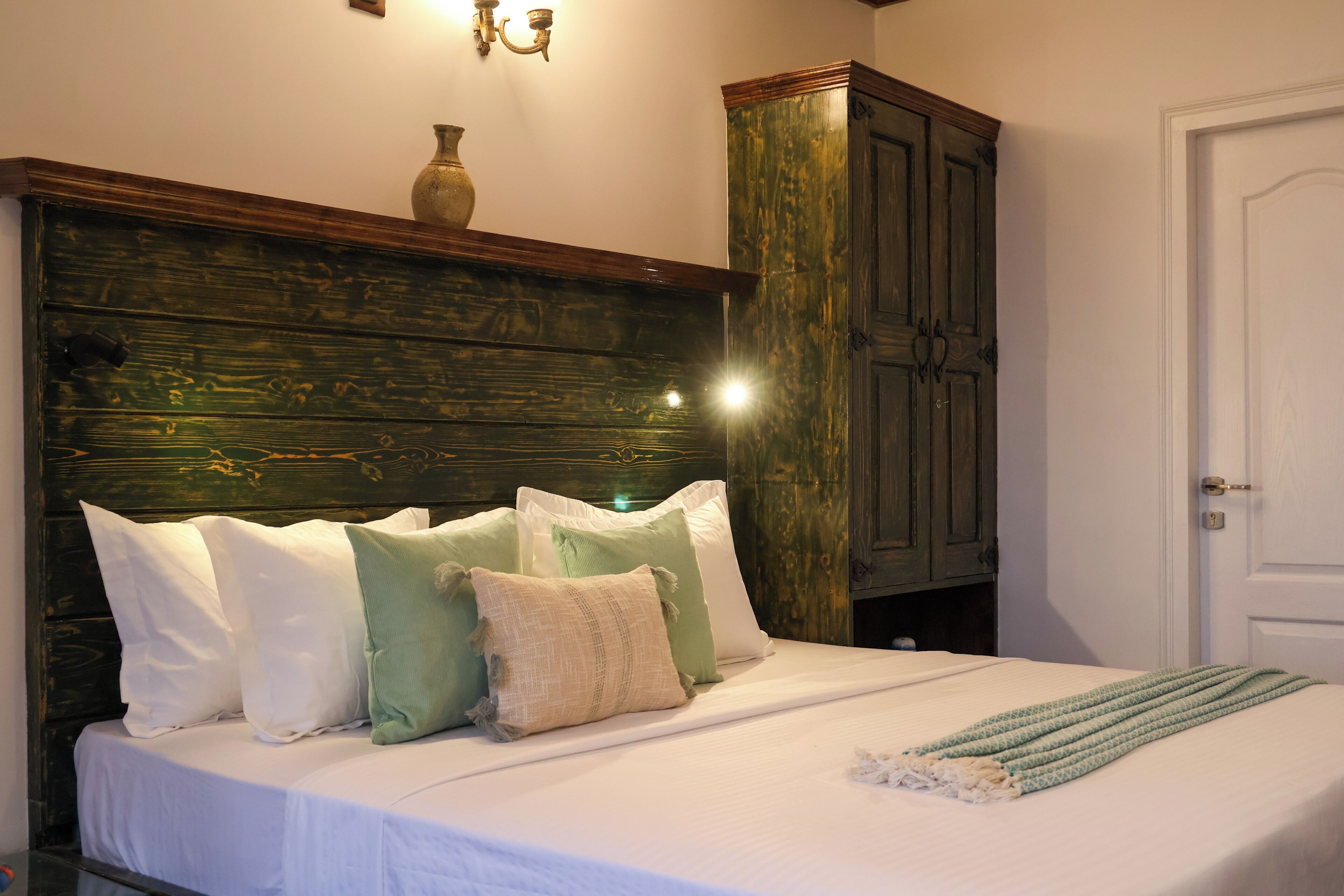 A bed with white bedding, multiple pillows, a green throw blanket, and a wooden headboard.