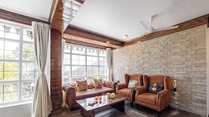 A room with a stone wall, leather sofas, a coffee table, and a ceiling fan. - Alaya Stays Farsauli 1 Pet friendly 3BHK (Nagri Gaon)