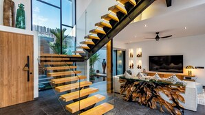 A modern interior with a wooden staircase, a large TV, and a unique wooden coffee table. - Villa Balinese Elite Sanctuary (Ubud)