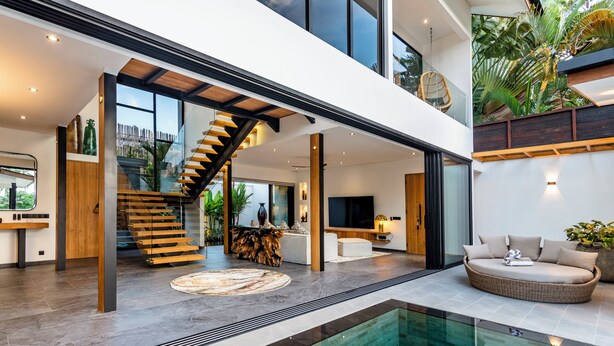 A modern interior with a glass-bottomed pool, a wooden staircase, and a seating area with a view of the outdoors. - Villa Balinese Elite Sanctuary (Ubud)