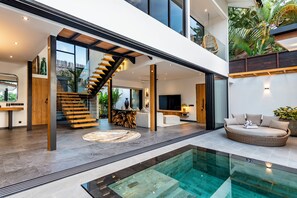 Ein modernes Interieur mit einem Pool mit Glasboden, einer Holztreppe und einer Sitzecke mit Blick ins Freie.