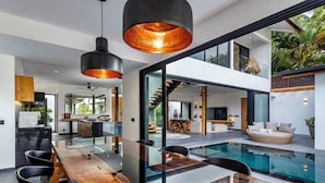 A modern interior with a glass dining table, black chairs, a pool, and a staircase leading to an upper level. - Villa Balinese Elite Sanctuary (Ubud)