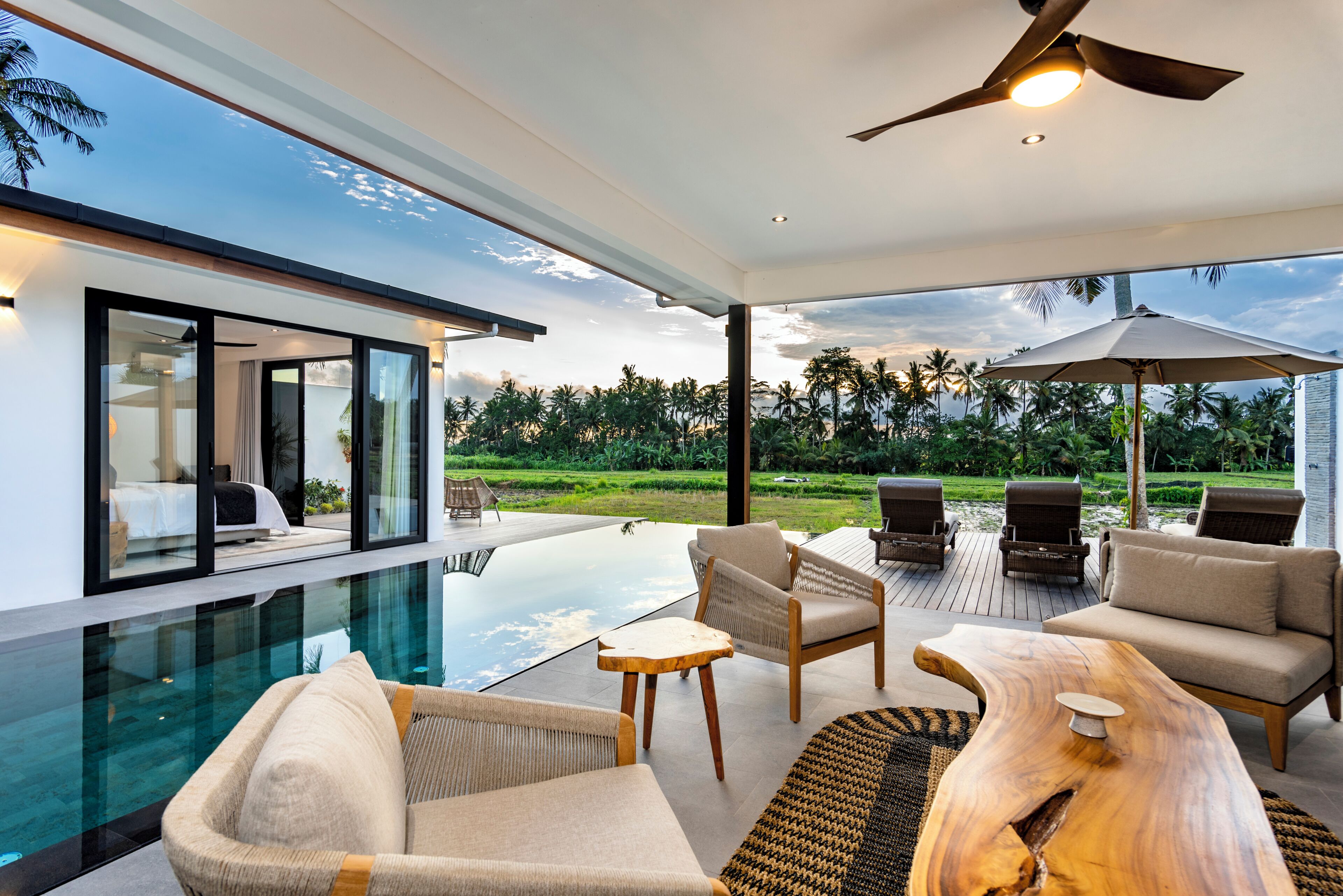 A modern indoor pool area with lounge chairs, a wooden coffee table, and a ceiling fan.
