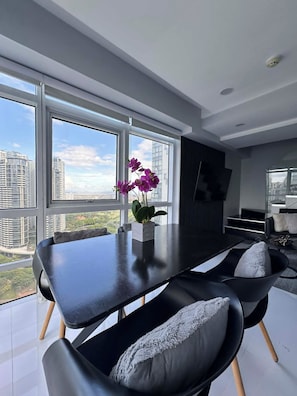 A modern dining area with a black table, two chairs, and a vase of purple flowers. - Hive Loft 2BR BGC w/ Free Parking + Skyline View (Taguig)