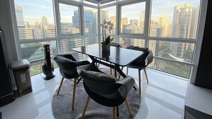 A modern dining area with a table and chairs, large windows with a city view, and a small side table with a speaker. - Hive Loft 2BR BGC w/ Free Parking + Skyline View (Taguig)